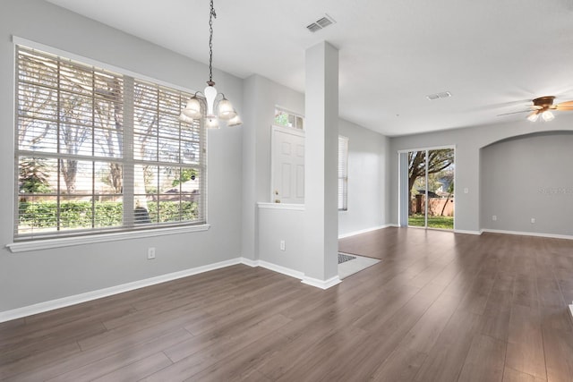 empty room featuring a ceiling fan, visible vents, baseboards, arched walkways, and dark wood-type flooring