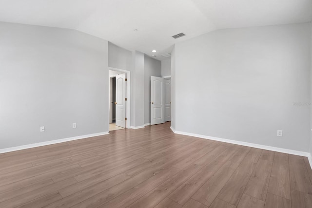 empty room with lofted ceiling, wood finished floors, visible vents, and baseboards