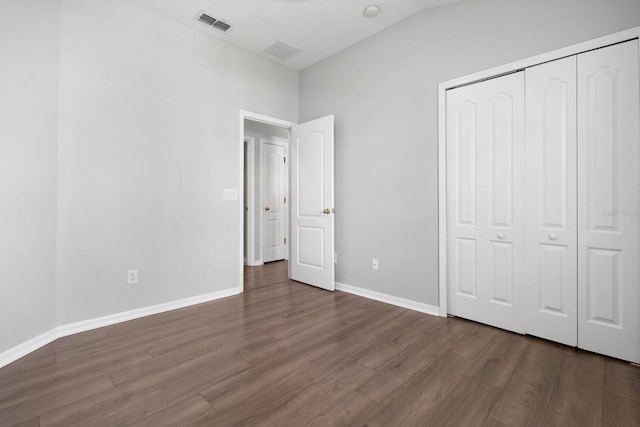 unfurnished bedroom featuring visible vents, baseboards, vaulted ceiling, wood finished floors, and a closet