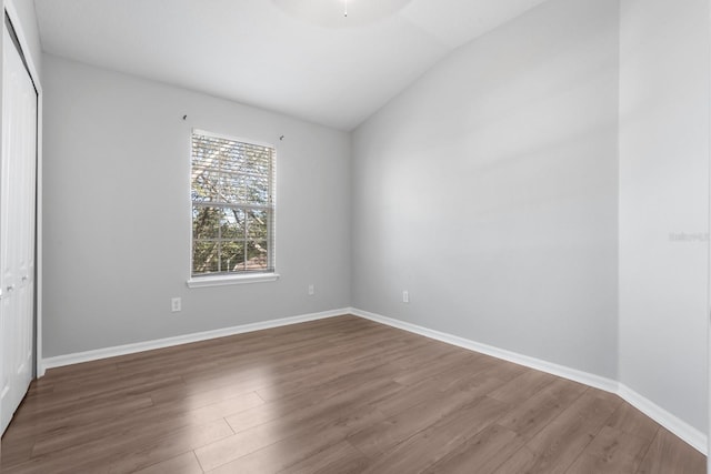 spare room featuring baseboards, lofted ceiling, and wood finished floors