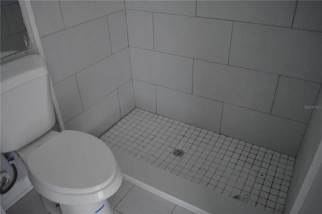 bathroom featuring toilet, tile patterned flooring, and a tile shower