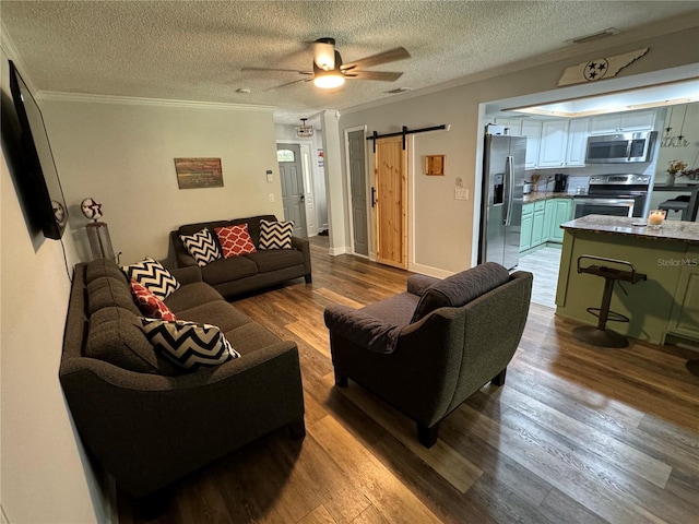 living room with ceiling fan, a barn door, light wood-type flooring, a textured ceiling, and ornamental molding