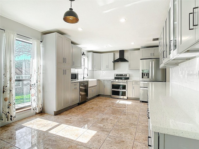 kitchen with wall chimney exhaust hood, gray cabinets, stainless steel appliances, and decorative light fixtures