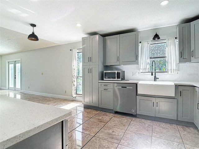 kitchen with gray cabinetry, decorative backsplash, pendant lighting, and appliances with stainless steel finishes