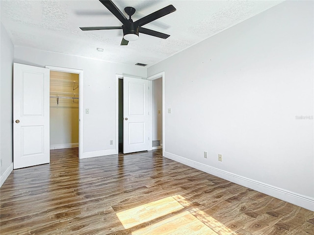 unfurnished bedroom featuring ceiling fan, dark hardwood / wood-style floors, a walk in closet, and a textured ceiling