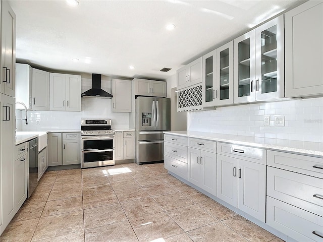 kitchen with wall chimney exhaust hood, stainless steel appliances, gray cabinets, decorative backsplash, and light tile patterned flooring