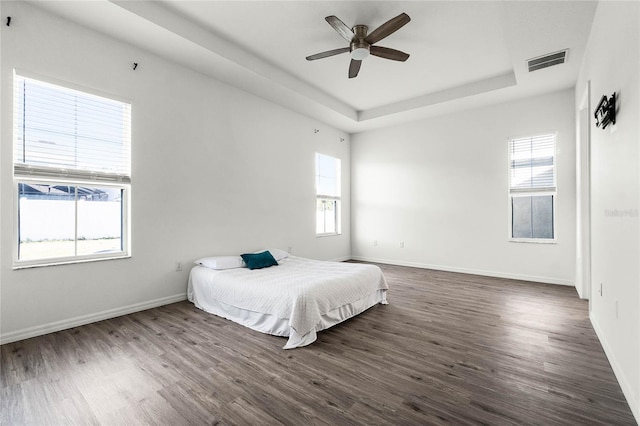 bedroom with a raised ceiling, multiple windows, ceiling fan, and dark wood-type flooring