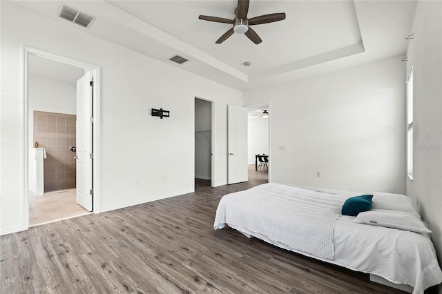 bedroom with ensuite bath, a tray ceiling, ceiling fan, hardwood / wood-style flooring, and a closet