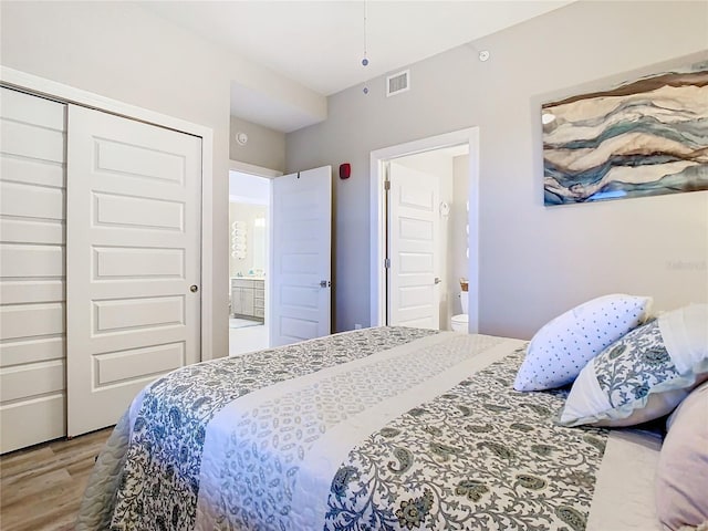 bedroom featuring wood-type flooring, a closet, and ensuite bath