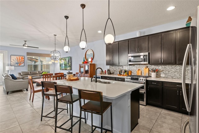 kitchen with sink, hanging light fixtures, a center island with sink, appliances with stainless steel finishes, and ceiling fan with notable chandelier