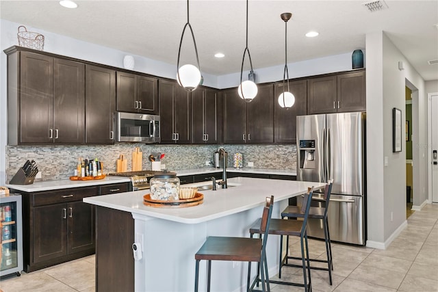 kitchen with pendant lighting, stainless steel appliances, a kitchen island with sink, and backsplash