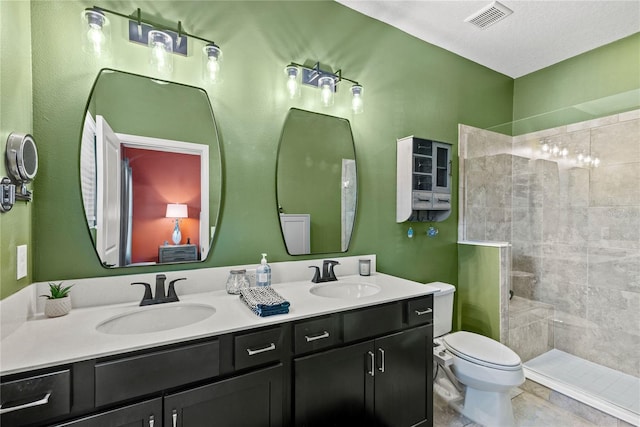 bathroom featuring toilet, double vanity, a tile shower, and a sink