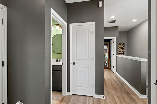 corridor featuring light wood finished floors, recessed lighting, visible vents, a sink, and baseboards