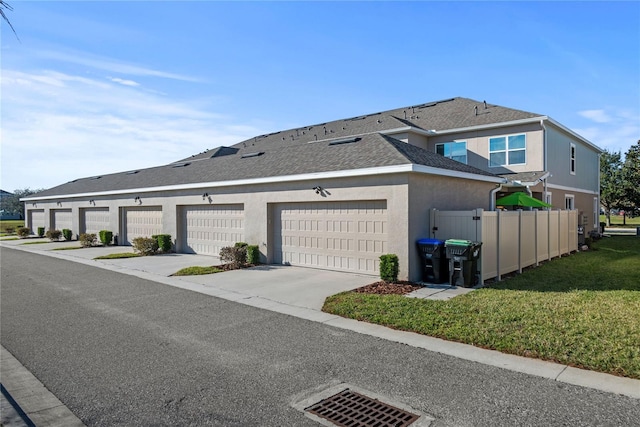 view of front of home featuring a garage, fence, roof with shingles, stucco siding, and a front yard