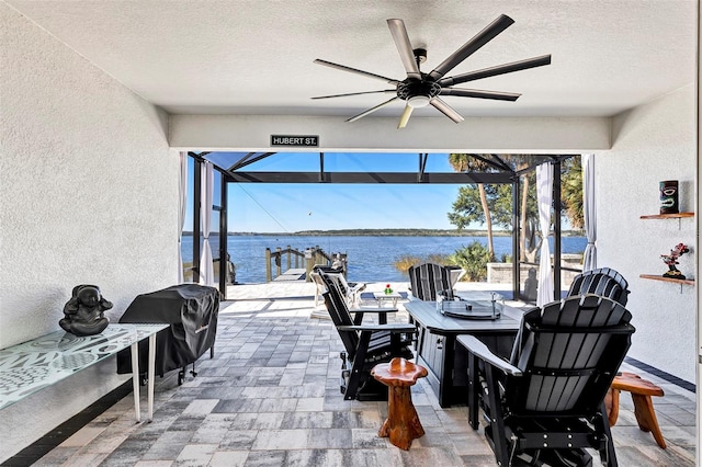 view of patio featuring ceiling fan, a water view, a grill, and glass enclosure