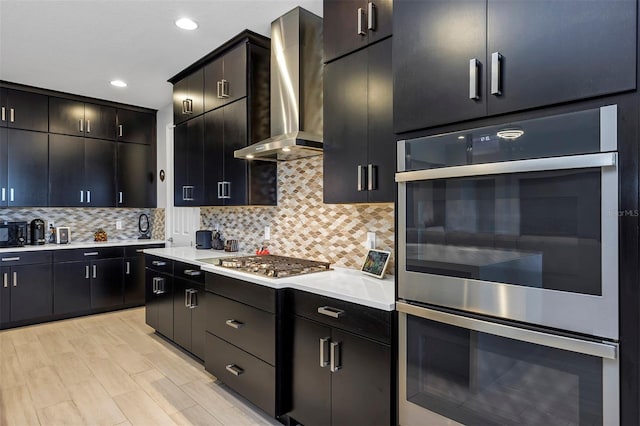 kitchen featuring appliances with stainless steel finishes, light hardwood / wood-style flooring, wall chimney range hood, and tasteful backsplash