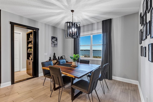 dining area with an inviting chandelier, light hardwood / wood-style floors, a textured ceiling, and a water view