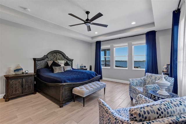 bedroom with a raised ceiling, a textured ceiling, ceiling fan, and a water view