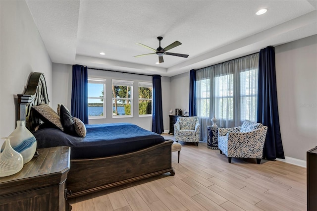 bedroom with a raised ceiling, ceiling fan, multiple windows, and light hardwood / wood-style flooring