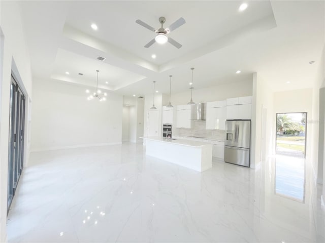 kitchen featuring a tray ceiling, white cabinetry, appliances with stainless steel finishes, wall chimney exhaust hood, and light countertops