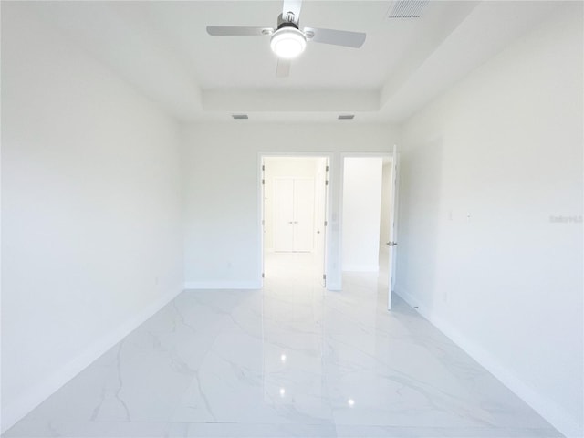 unfurnished room with visible vents, a raised ceiling, marble finish floor, a ceiling fan, and baseboards