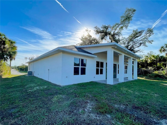 view of side of home with a yard, a patio area, central AC, and stucco siding