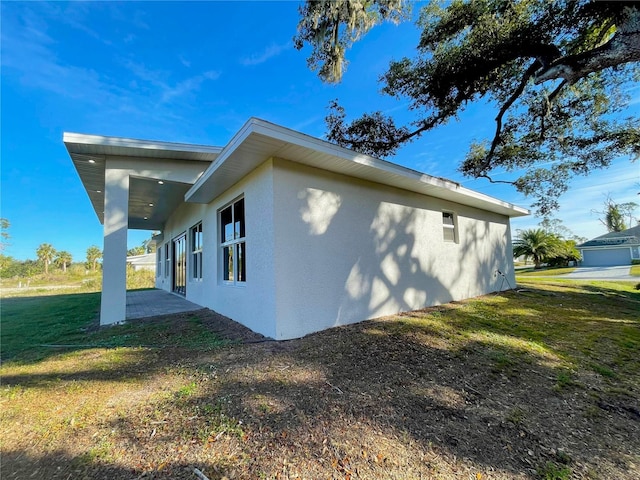 view of side of home featuring stucco siding, a lawn, and a patio