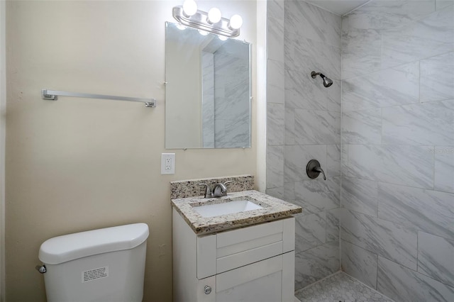 bathroom with toilet, a tile shower, and vanity