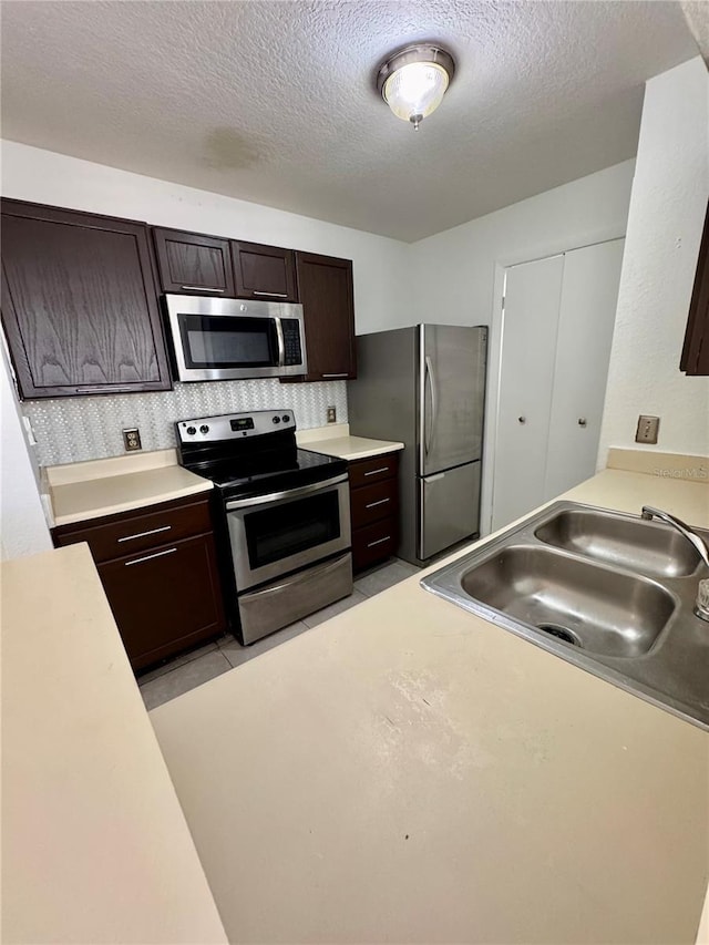 kitchen with appliances with stainless steel finishes, a textured ceiling, dark brown cabinets, and sink