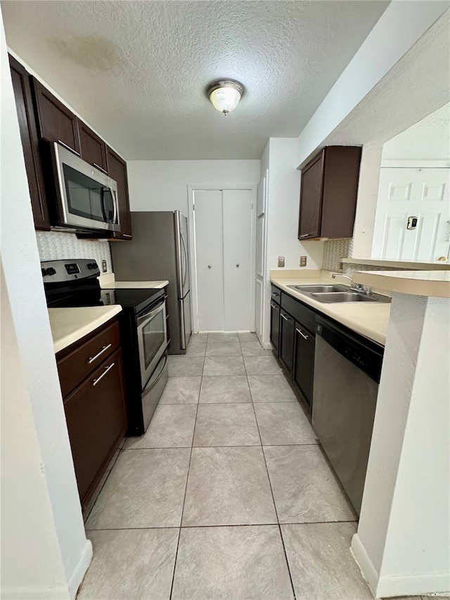 kitchen with dark brown cabinetry, sink, light tile patterned floors, and stainless steel appliances