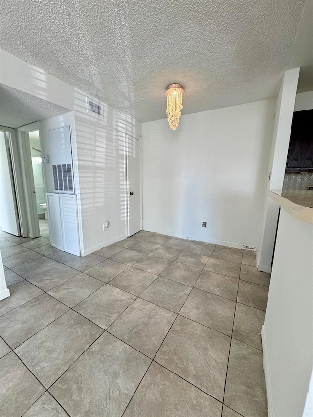 tiled empty room with a textured ceiling and a notable chandelier