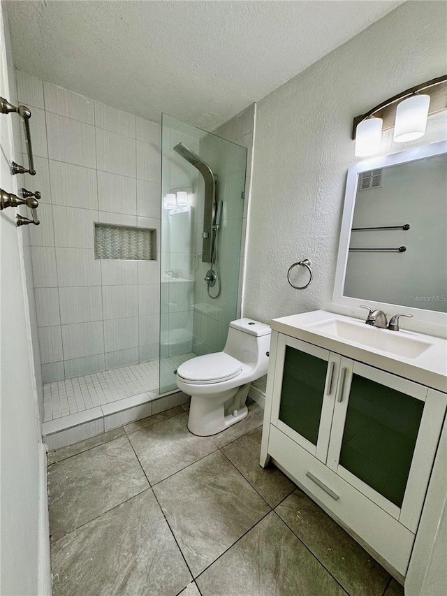 bathroom with tiled shower, vanity, a textured ceiling, and toilet