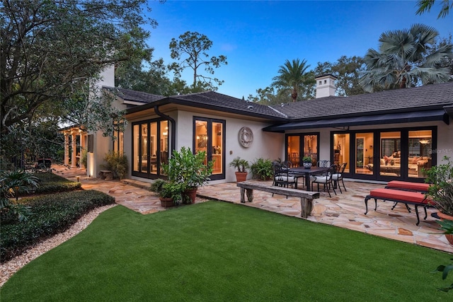 rear view of property featuring french doors, a patio area, and a lawn