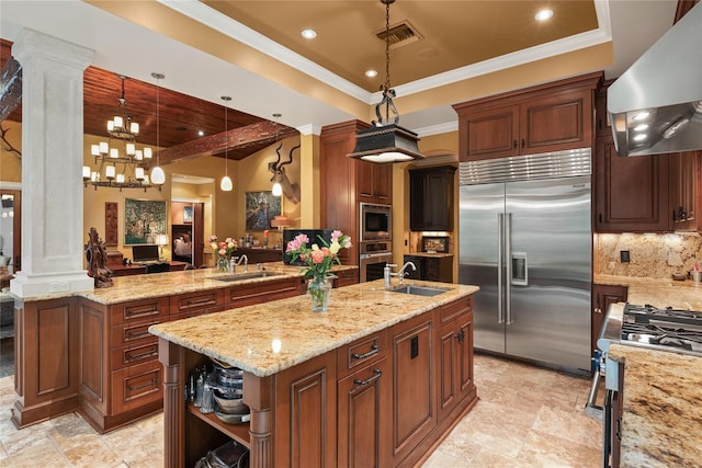 kitchen with ornate columns, built in appliances, pendant lighting, extractor fan, and a center island with sink