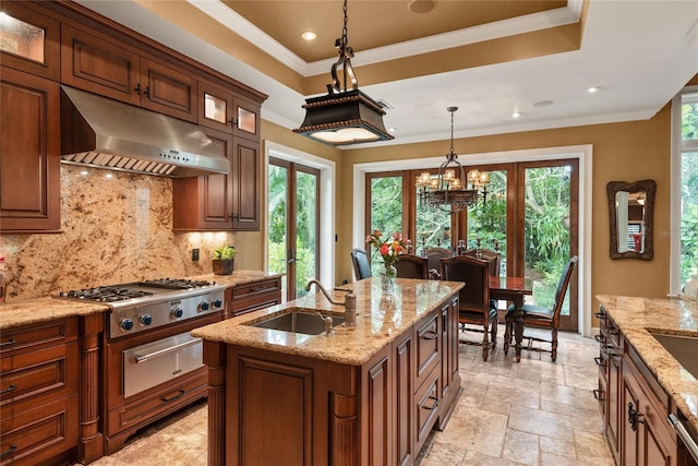 kitchen with french doors, backsplash, light stone counters, sink, and an island with sink