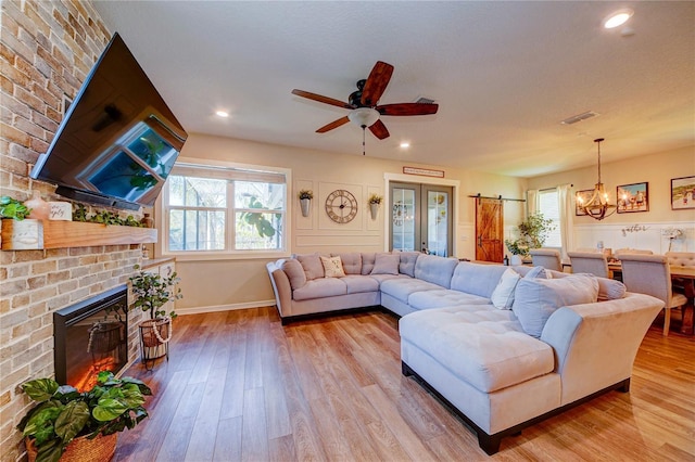 living room with ceiling fan with notable chandelier, light wood-type flooring, a fireplace, and a wealth of natural light