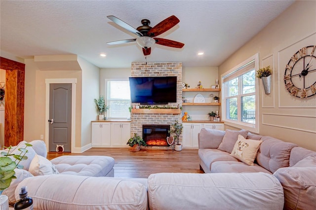 living room with ceiling fan, a fireplace, a textured ceiling, and light wood-type flooring