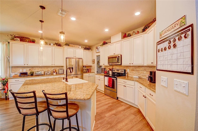 kitchen with appliances with stainless steel finishes, light stone counters, a center island with sink, light hardwood / wood-style flooring, and white cabinets