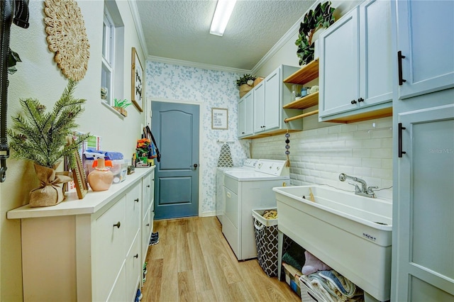 washroom featuring cabinets, independent washer and dryer, a textured ceiling, ornamental molding, and light hardwood / wood-style floors