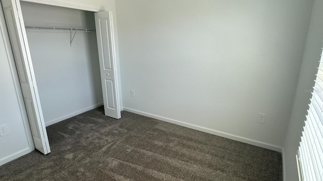 unfurnished bedroom with dark carpet and a closet