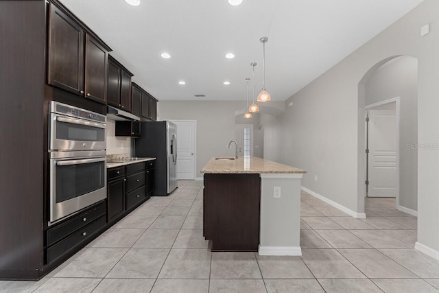 kitchen featuring sink, stainless steel appliances, light stone counters, an island with sink, and pendant lighting