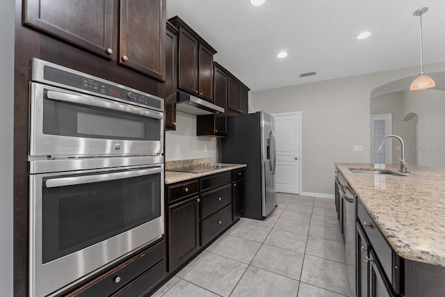 kitchen with light stone countertops, appliances with stainless steel finishes, dark brown cabinetry, sink, and hanging light fixtures