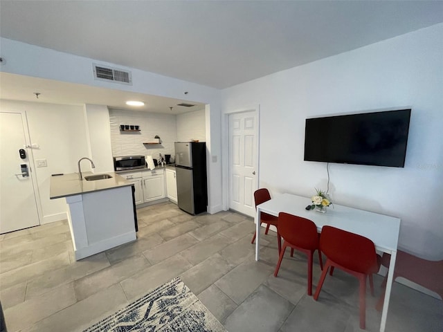 kitchen featuring kitchen peninsula, stainless steel appliances, white cabinetry, and sink