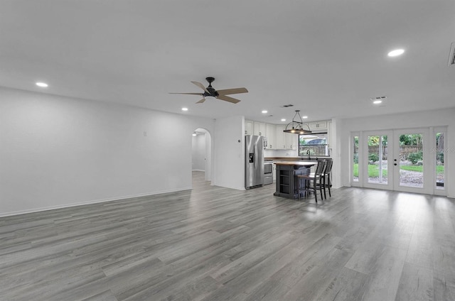 unfurnished living room with ceiling fan, light hardwood / wood-style floors, sink, and french doors