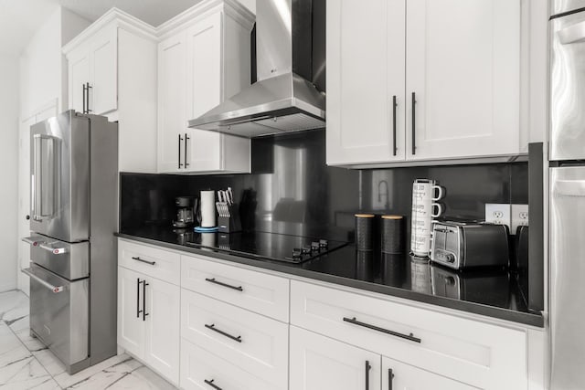 kitchen with stainless steel fridge, high end fridge, black electric cooktop, wall chimney range hood, and white cabinetry