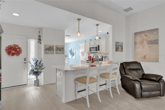 kitchen with white cabinets, a kitchen breakfast bar, hanging light fixtures, appliances with stainless steel finishes, and kitchen peninsula