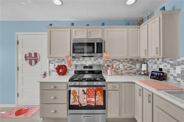 kitchen featuring a textured ceiling, backsplash, stainless steel appliances, and white cabinetry