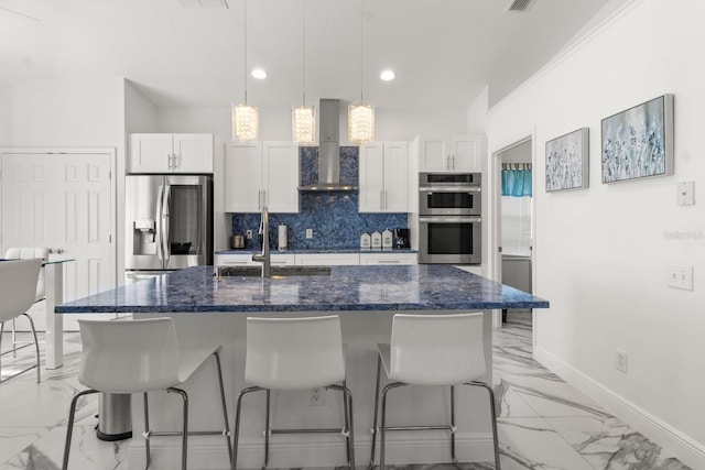 kitchen with white cabinetry, wall chimney exhaust hood, stainless steel appliances, tasteful backsplash, and a center island with sink