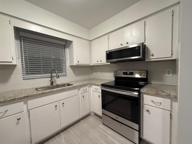 kitchen with appliances with stainless steel finishes, backsplash, light stone counters, sink, and white cabinetry