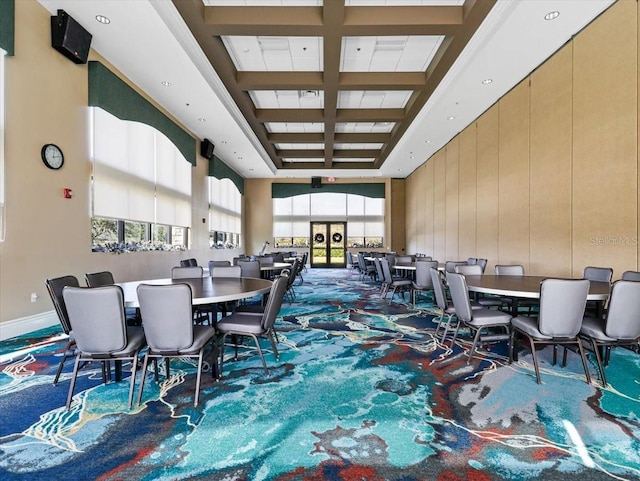 carpeted dining area with wooden walls, coffered ceiling, and a high ceiling